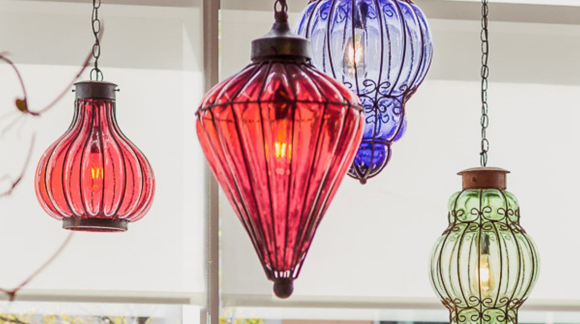Hand blown glass lanterns in ruby, cobalt and sea glass hanging on chains above the ROAM dining room, each lit by a warm filament bulb.