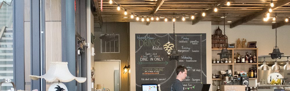 A ROAM cook working behind the pass beneath handwritten chalkboard menus, with string lights along the ceiling.